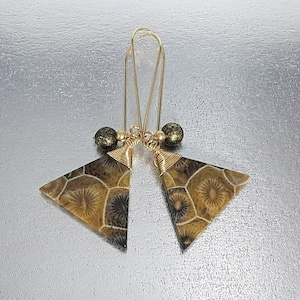 Könnte beinhalten: Goldene Ohrringe mit einem dreieckigen Anhänger mit einem braunen und goldenen versteinerten Muster. Der Anhänger ist mit einer kleinen goldenen Perle verziert.