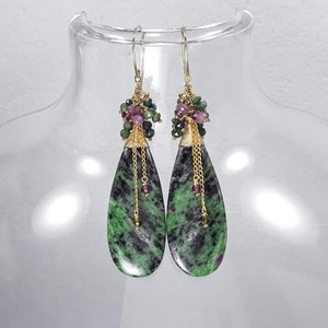 May include: A pair of green and black teardrop-shaped earrings with gold accents and pink and green gemstone beads.