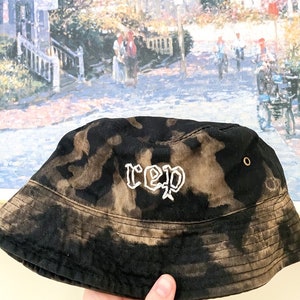 May include: Black bucket hat with a white "rep" embroidered on the front. The hat has a tie-dye pattern.