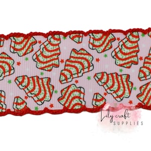 May include: A light pink ribbon featuring a repeating pattern of stylized Christmas trees with red and green stripes, accented by small red and green stars. The ribbon edges are finished with a decorative red scalloped crochet trim.