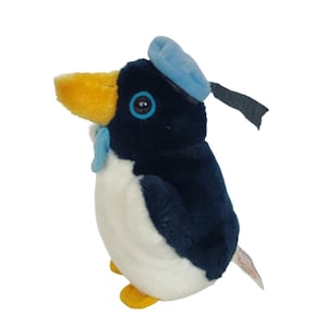 Puede incluir: Un juguete de peluche de pingüino azul y blanco que lleva un sombrero azul con una visera negra. El pingüino tiene un pico amarillo y ojos azules.