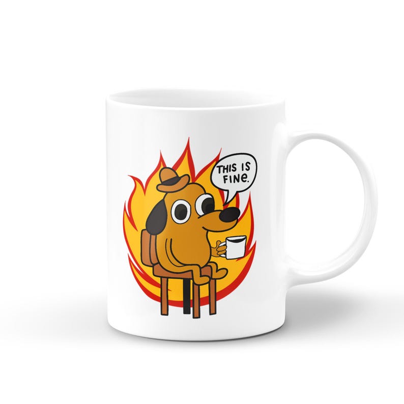 May include: White ceramic coffee mug with a cartoon dog sitting in a chair surrounded by flames. The dog is wearing a hat and holding a cup of coffee. The text "This is fine." is in a speech bubble above the dog.