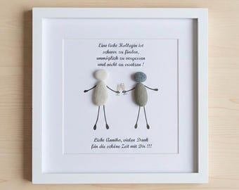 Può includere: Una cornice bianca quadrata contenente un'opera d'arte in sassi raffigurante due figure che tengono in mano dei calici da champagne. Il testo recita: Eine liebe Kollegin ist schwer zu finden, unmöglich zu vergessen und nicht zu ersetzen! Liebe Annika, vielen Dank für die schöne Zeit mit Dir !!!