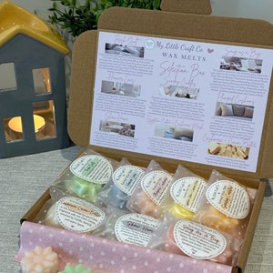May include: A selection box of scented wax melts in a variety of fragrances, including "Fresh Out", "Sunday Cuddles", "Show Home", "Snug As A Bug", "Plumped Cushions", "Cashmere Cocoa & Butter", "Honey Lives", and "Egyptian Cotton & Cashmere Musk". The box is open and the wax melts are visible.