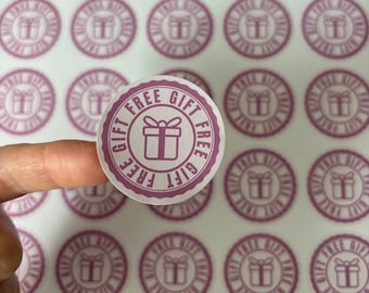 May include: A sheet of pink and white round stickers with the text "FREE GIFT" in a circle around a gift box icon. The stickers are designed for use on products or packaging.