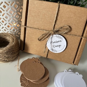 May include: A brown cardboard box tied with twine and a gift tag that reads "Mandarin Orange". The box is surrounded by a pile of brown round gift tags and a pile of white round gift tags.