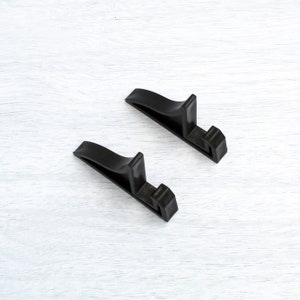 May include: Two black plastic display stands for books, photos, or other items. The stands are shaped like an upside-down 'L' and are made of a sturdy plastic.