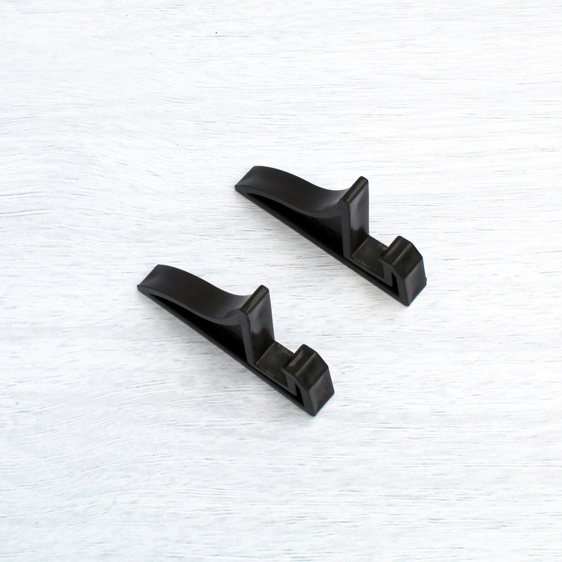 May include: Two black plastic display stands for books, photos, or other items. The stands are shaped like an upside-down 'L' and are made of a sturdy plastic.