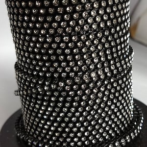 May include: A roll of black rhinestone trim with clear rhinestones. The trim is on a spool and is ready to be used for crafting or decorating.