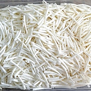 May include: A clear plastic container filled with numerous white, julienned vegetables. The vegetables are cut into thin, uniform strips, creating a dense, textured pattern. The container has a green latch on the side.