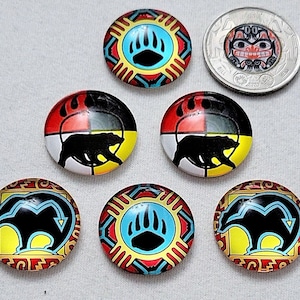 May include: Six round glass cabochons with colourful designs featuring a black bear silhouette and paw print. The designs are inspired by Native American art.