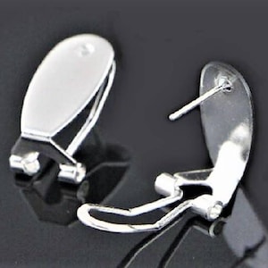 May include: A pair of silver-toned earring backs with a clip-on design. The backs are oval-shaped and have a smooth, shiny finish.