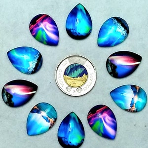 Peut inclure: Dix cabochons en verre iridescent en forme de larme avec un motif aurora borealis bleu, vert et rose. Les cabochons sont disposés en cercle autour d'une pièce canadienne de deux dollars avec une image de l'aurore boréale.