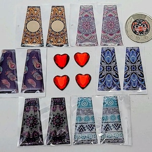 Peut inclure: Assortiment de supports d'oreille en tissu à motifs colorés, avec des embellissements en résine en forme de cœur rouge. Les supports d'oreille sont de différents motifs géométriques et floraux.