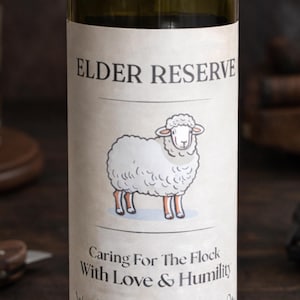 May include: A wine bottle with a label that reads "ELDER RESERVE" above a cartoon sheep illustration. Below the sheep, the label says "Caring For The Flock With Love & Humility We Appreciate All You". The bottle is green.