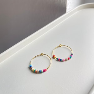 May include: A pair of gold hoop earrings with colourful beads. The beads are a mix of pink, blue, green, yellow, and white.