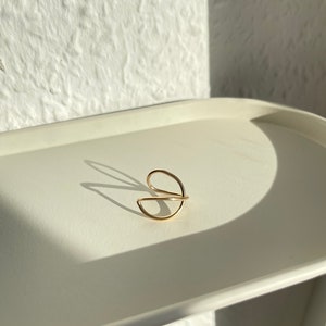 Puede incluir: Un anillo de color dorado con un diseño simple y moderno. El anillo está hecho de dos bandas finas que están entrelazadas.