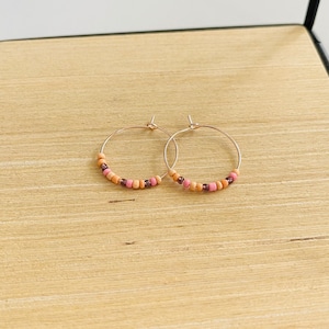 Könnte beinhalten: Ein Paar Creolen mit einem Perlenmuster. Die Perlen sind in den Farben Pfirsich und Rosa gehalten.