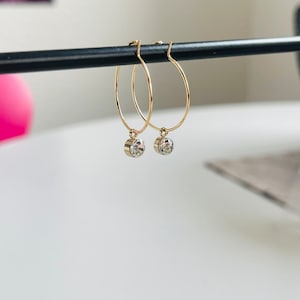 Puede incluir: Un par de pendientes de aro de oro con un pequeño cristal transparente que cuelga de cada aro.