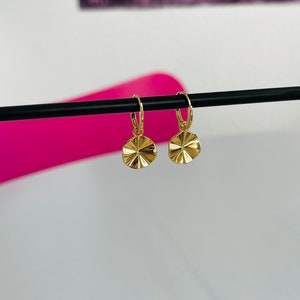 Könnte beinhalten: Ein Paar goldene Creolen mit einem kleinen, strukturierten, runden Anhänger, der an jedem Creolen hängt.