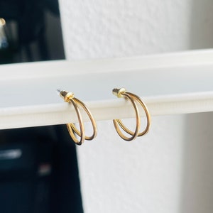 Könnte beinhalten: Ein Paar goldene Creolen mit einem Doppelring-Design. Die Ohrringe sind schlicht und elegant.