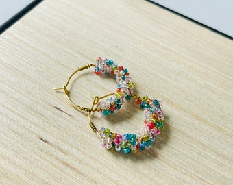 May include: A pair of gold hoop earrings with colourful beads. The beads are a mix of pink, blue, green, and orange.
