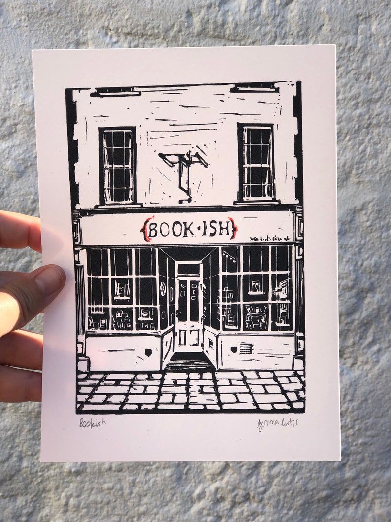 May include: Black and white linocut print of a shop front with the text "BOOK.ISH" above the door. The print is signed "Bookish" and "Gemma Cutts" in the bottom corners.