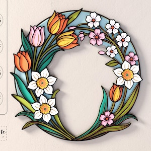 May include: A vibrant floral wreath design with tulips, daffodils, and other flowers in orange, pink, and white. The wreath has a light blue background and green leaves. The image includes the text "SVG", "DXF", "EPS", "PDF", and "CutCute paper".