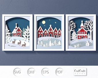 May include: Three white frames with a winter village scene inside. The frames are on a blue background. The scenes include a church, houses, trees, deer, and a snowman.