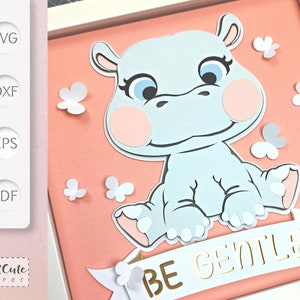 May include: A light blue hippopotamus sitting on a pink background with a white banner that reads 'BE GENTLE' in gold letters. The hippopotamus has pink cheeks and white flowers are scattered around the hippopotamus.