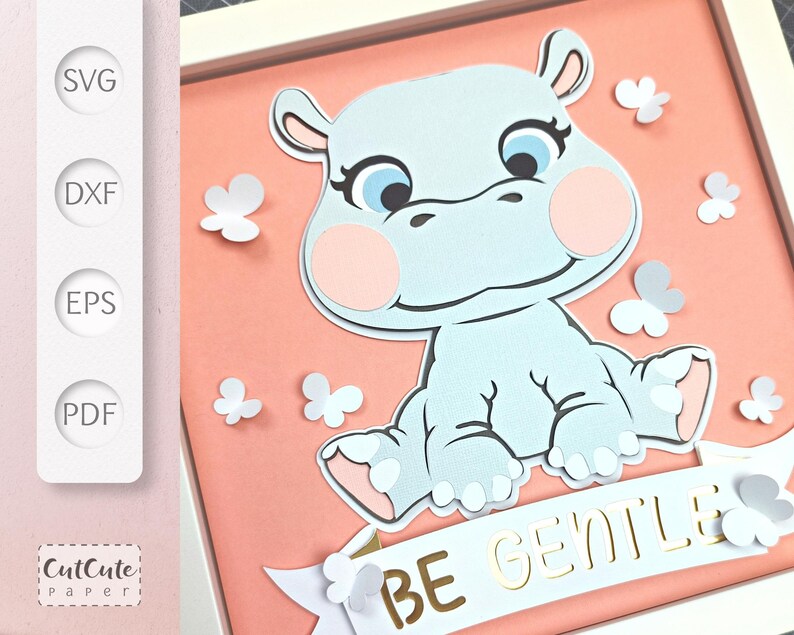 May include: A light blue hippopotamus sitting on a pink background with a white banner that reads 'BE GENTLE' in gold letters. The hippopotamus has pink cheeks and white flowers are scattered around the hippopotamus.