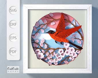 May include: A red bird with black eyes and a black beak flies over a branch of pink cherry blossoms. The background is a blue and pink sunset with white clouds. The image is framed in a white frame.