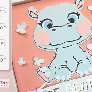May include: A light blue hippopotamus with pink cheeks and eyelashes. The hippopotamus is sitting on a peach background with white butterflies. The hippopotamus is holding a white banner with the words 'Be Gentle' in gold letters.