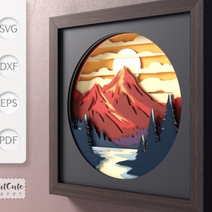 May include: A papercraft mountain scene with a red mountain, blue trees, and a yellow sun in a circular frame. The frame is brown wood with a black mat.