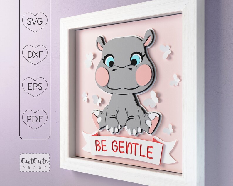 May include: A white framed picture with a pink background. The picture features a gray hippopotamus with pink cheeks and blue eyes. The hippopotamus is sitting on a white ribbon with the words 'BE GENTLE' in red letters. There are white butterflies scattered around the hippopotamus.