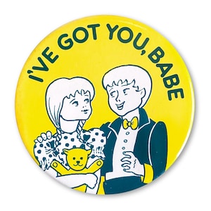 Może przedstawiać: Żółta przypinka z zielonym napisem "I'VE GOT YOU, BABE". Przypinka przedstawia kreskówkową ilustrację chłopca i dziewczynki, z dziewczynką trzymającą misia. Chłopiec ma na sobie smoking.