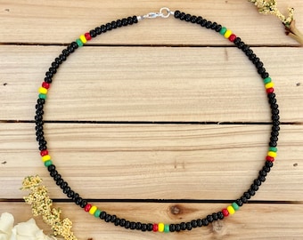 May include: A black beaded necklace with red, yellow, and green accents. The necklace is on a wooden surface.