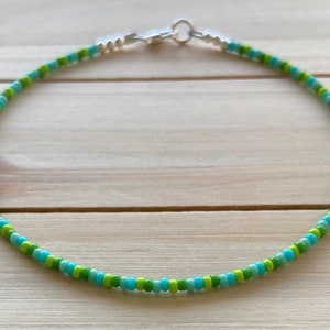 Puede incluir: Un delicado collar de cuentas con cuentas verdes y azules alternadas. El collar tiene un cierre plateado.