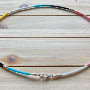 May include: A colorful beaded necklace with alternating colors of yellow, white, black, turquoise, and pink. The necklace has a silver clasp.