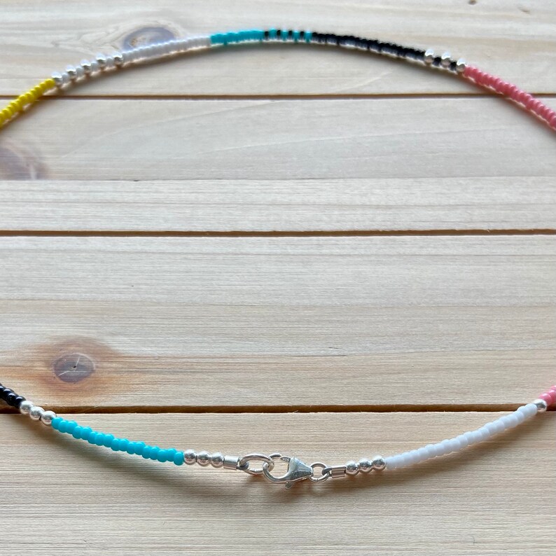 May include: A colorful beaded necklace with alternating colors of yellow, white, black, turquoise, and pink. The necklace has a silver clasp.