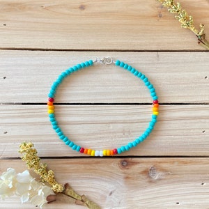 May include: A turquoise beaded necklace with a silver clasp. The necklace has a rainbow of colored beads in the center, including red, orange, yellow, white, and orange.