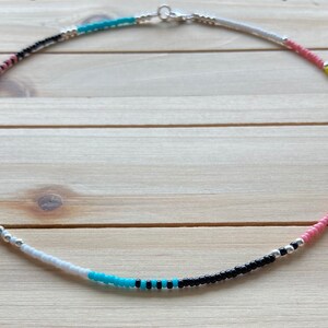 May include: A colorful beaded necklace with black, white, pink, and turquoise beads. The necklace is made with small, round beads and has a silver clasp.