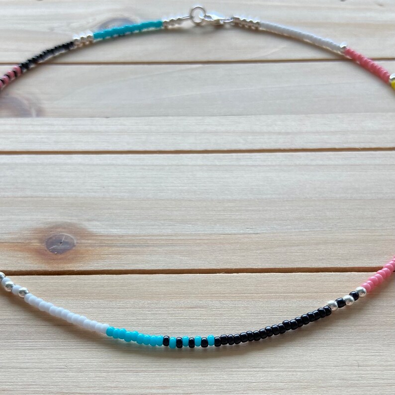 May include: A colorful beaded necklace with black, white, pink, and turquoise beads. The necklace is made with small, round beads and has a silver clasp.