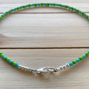 Puede incluir: Un collar de cuentas verde y azul con un cierre plateado.
