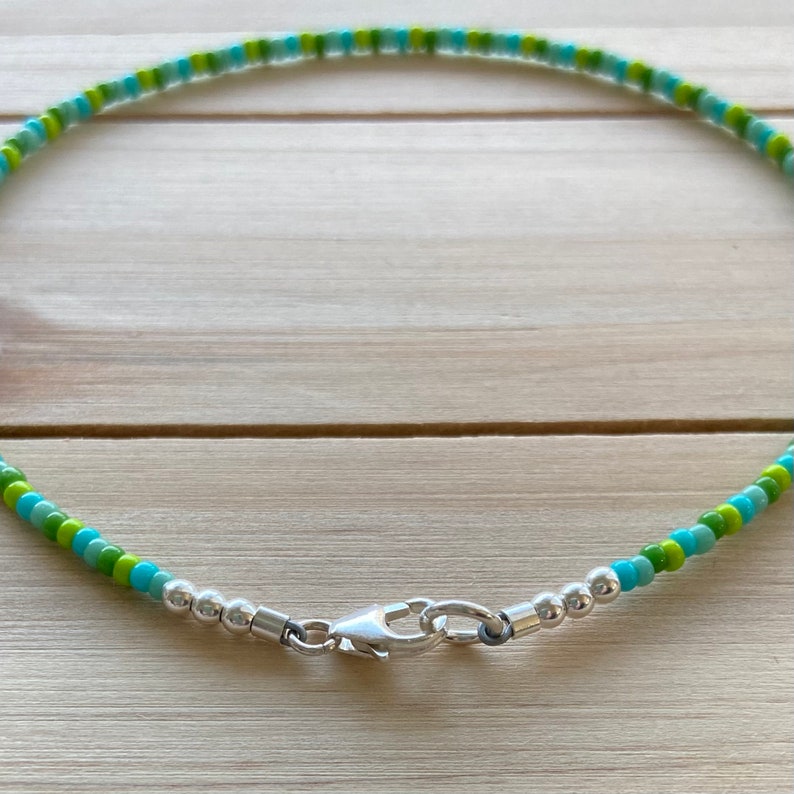 Puede incluir: Un collar de cuentas verde y azul con un cierre plateado.