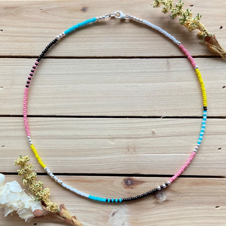 May include: A colorful beaded necklace with alternating pink, yellow, white, turquoise, and black beads. The necklace has a silver clasp.