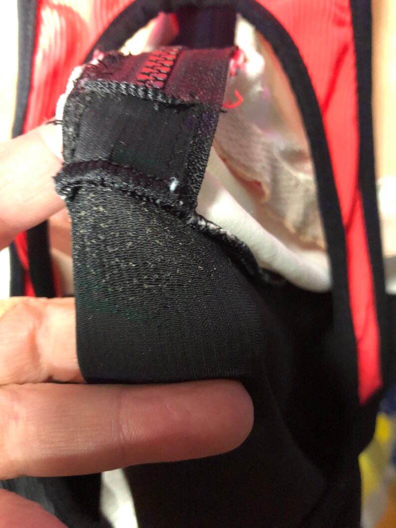 May include: Close-up of black fabric with a textured surface, possibly part of a garment. The fabric is folded over, revealing a red and white interior. The image highlights the stitching and construction details.