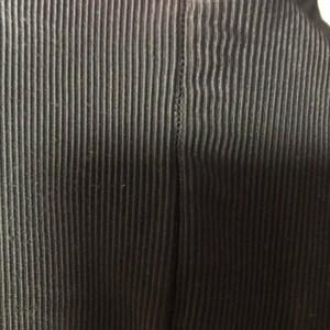 May include: Close-up of a black, vertically ribbed fabric. The fabric has a textured appearance with evenly spaced, raised lines. The image focuses on the detail of the material, highlighting the pattern and the dark color.