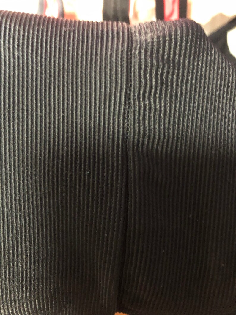 May include: Close-up of a black, vertically ribbed fabric. The fabric has a textured appearance with evenly spaced, raised lines. The image focuses on the detail of the material, highlighting the pattern and the dark color.