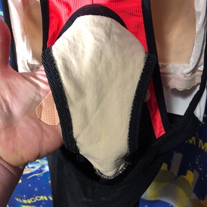 May include: Close-up of a black and coral athletic garment with a beige interior lining. The garment has a ribbed texture and black trim. The image shows a portion of the garment, highlighting its design and construction.